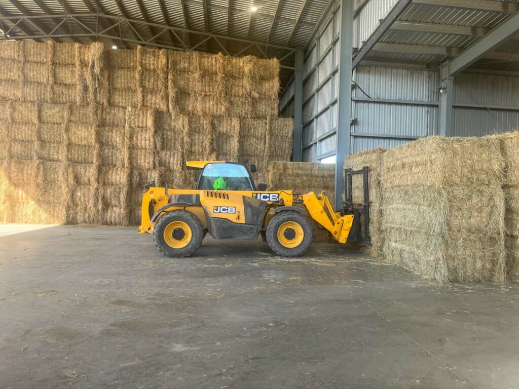 A yellow tractor is parked next to hay bales.