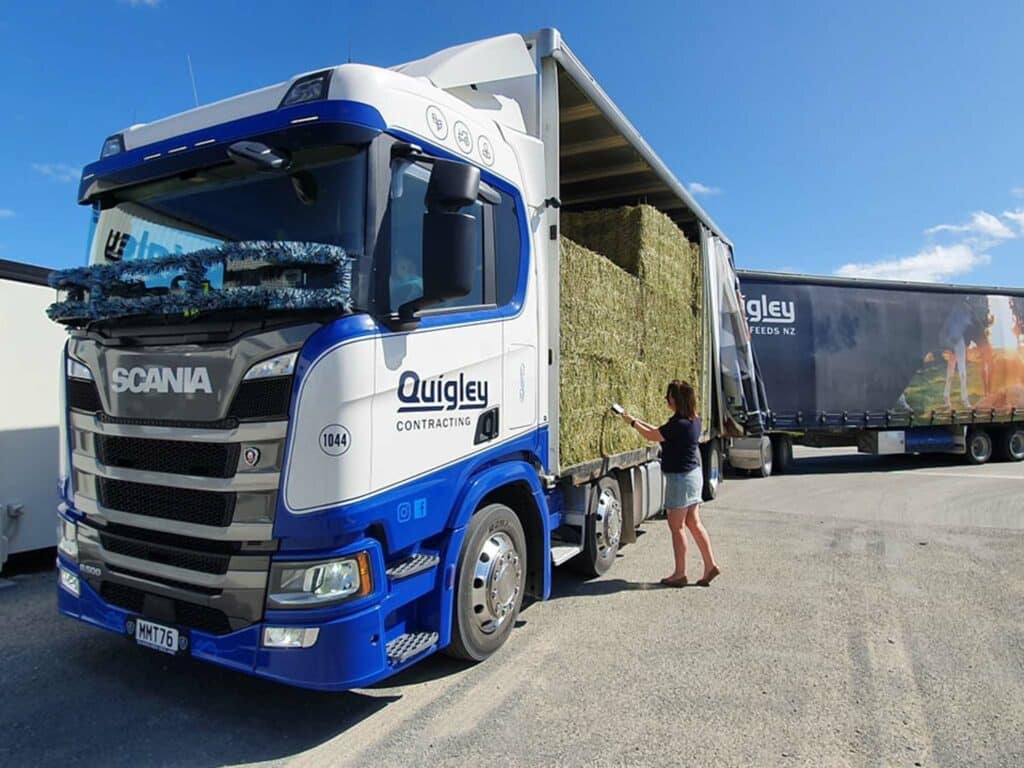 A woman loading hay into a semi truck.