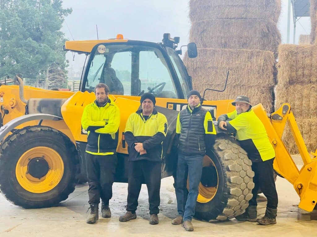 Four men standing in front of a tractor with hay bales.